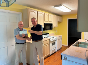 Two men standing in a kitchen exchanging a rent check and keys. 