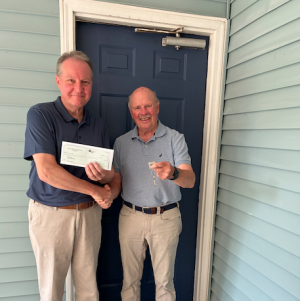 Two men standing in front of a blue door exchanging keys and a check payment for rent.